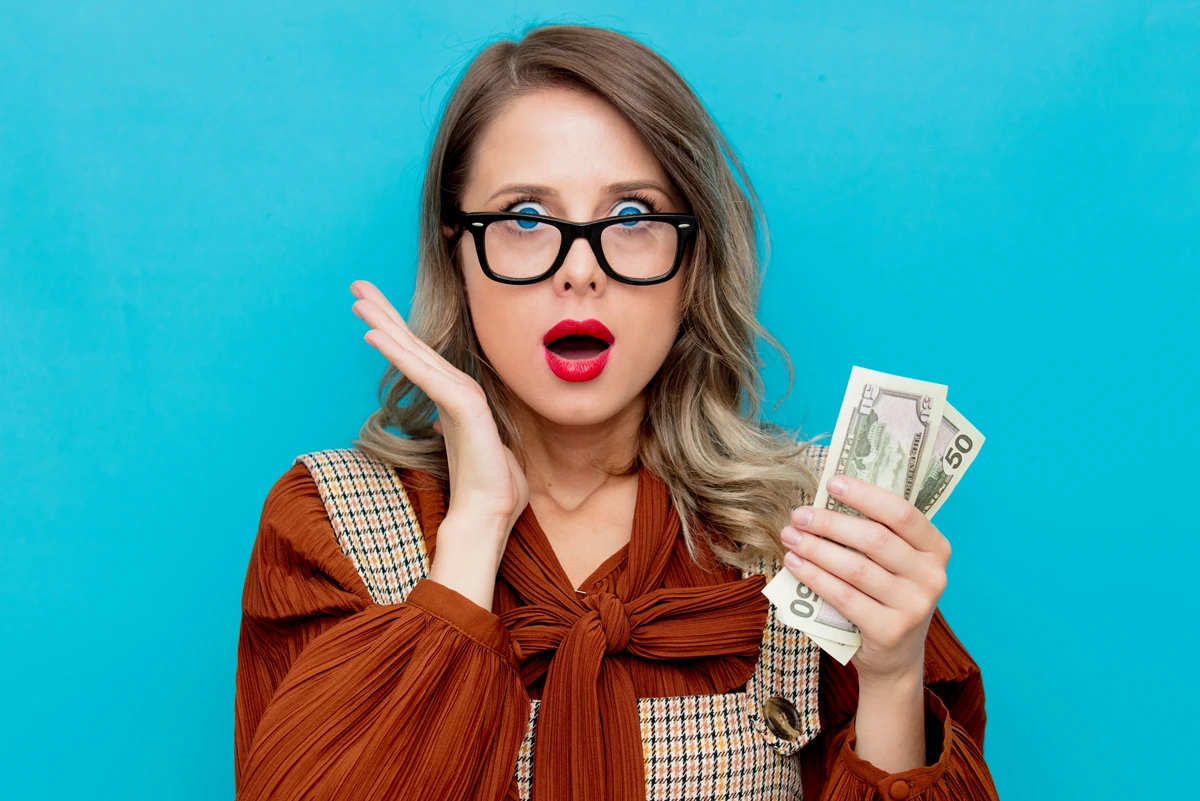 Surprised woman holding money, blue background.