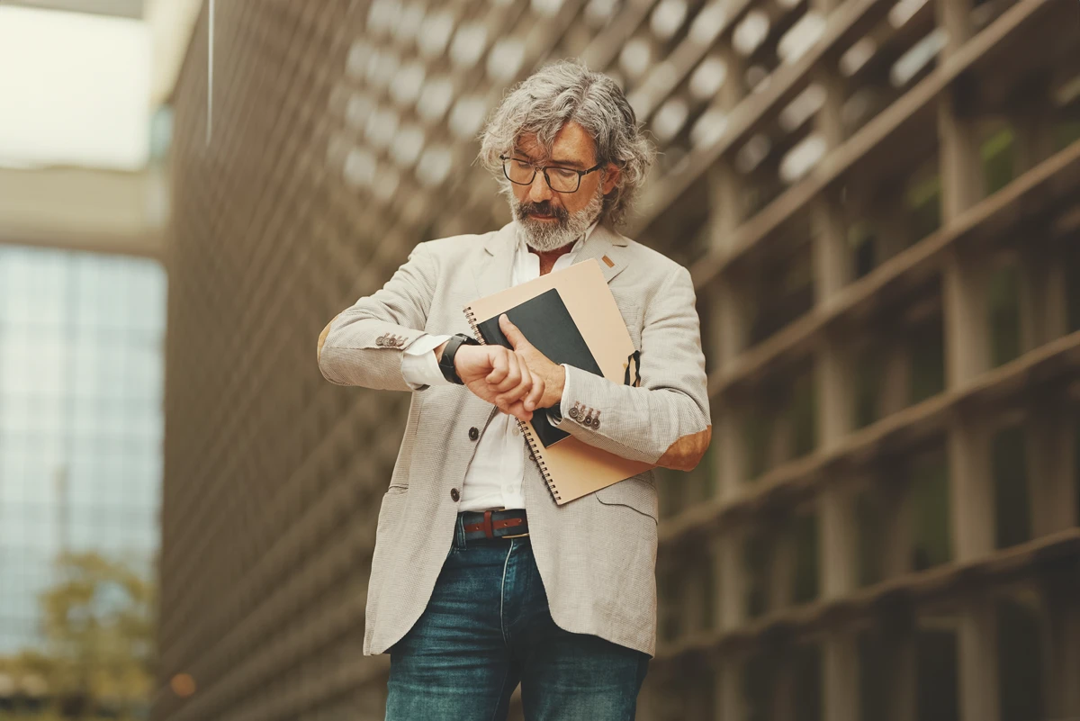 Mature man checking watch, holding documents, urban background.