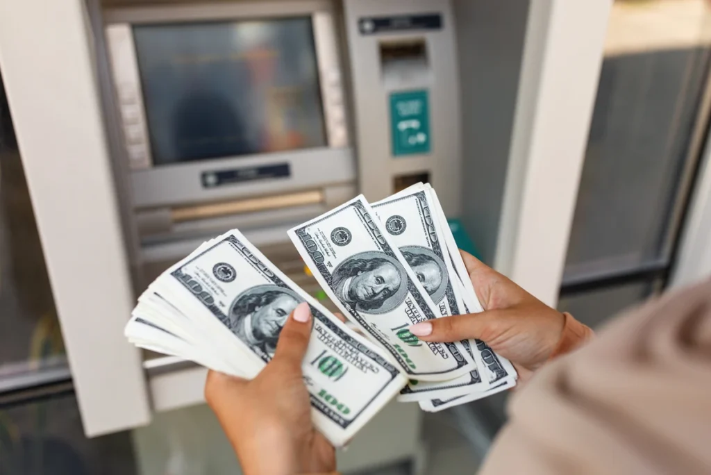 Person holding cash in front of ATM machine.