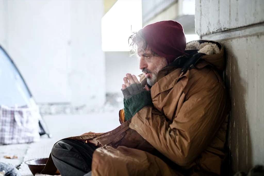 Homeless person keeping warm with a coat on street.