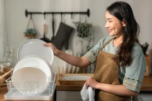 Woman drying and placing dishes in kitchen rack.