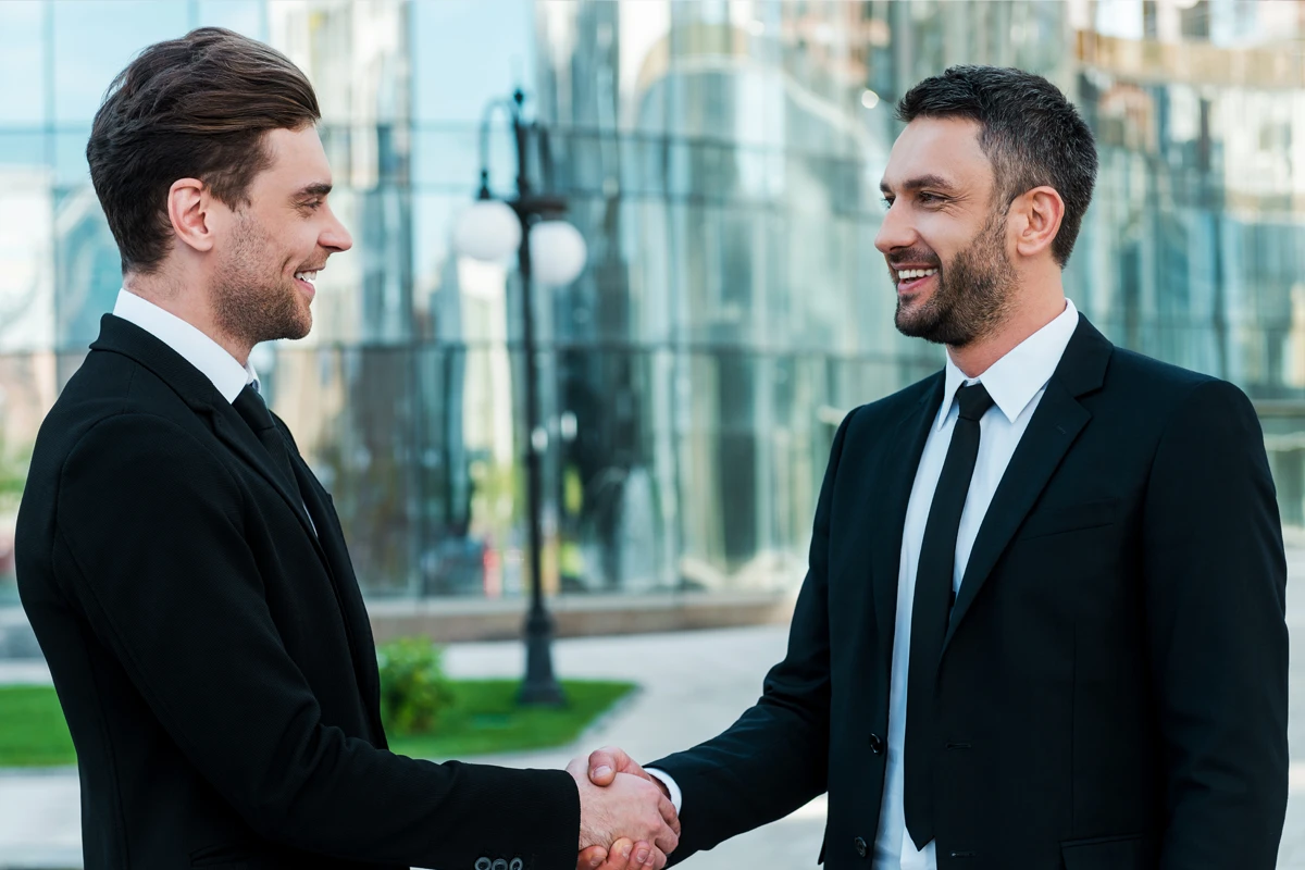 Two businessmen shaking hands in urban setting.