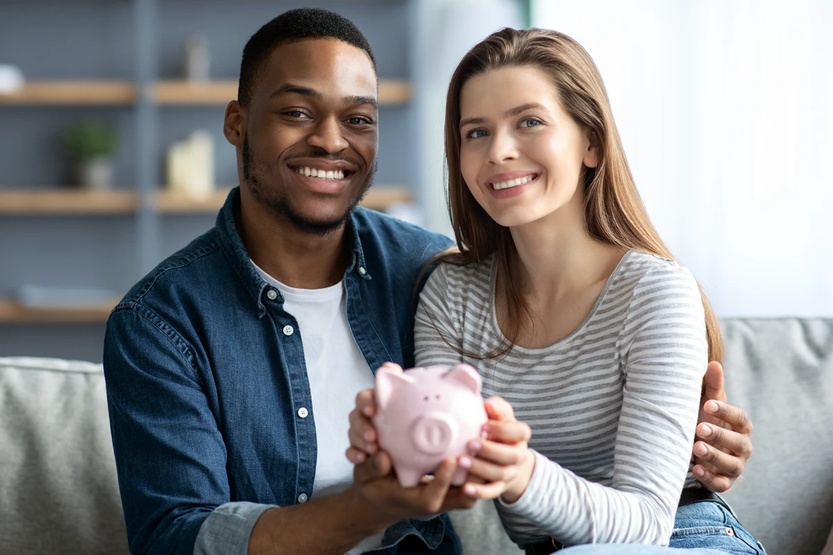 Couple smiling holding a piggy bank together.