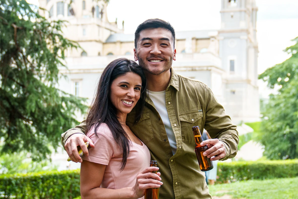 Happy couple toasting beers in a park.