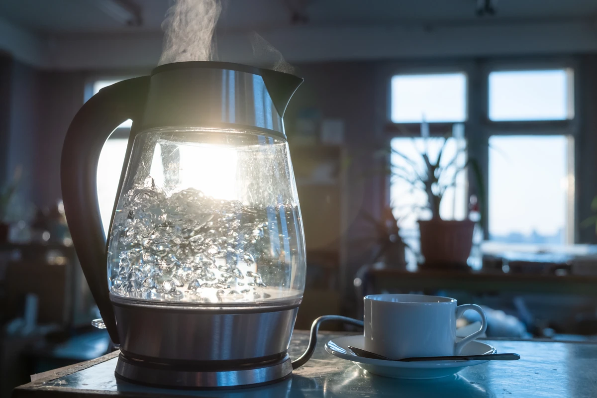 Steaming electric kettle heat sunrise with cup on table.