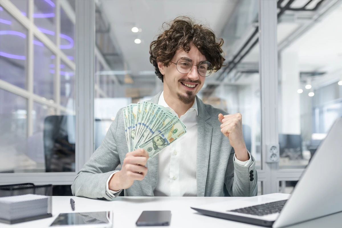 Joyful man holding money in modern office setting