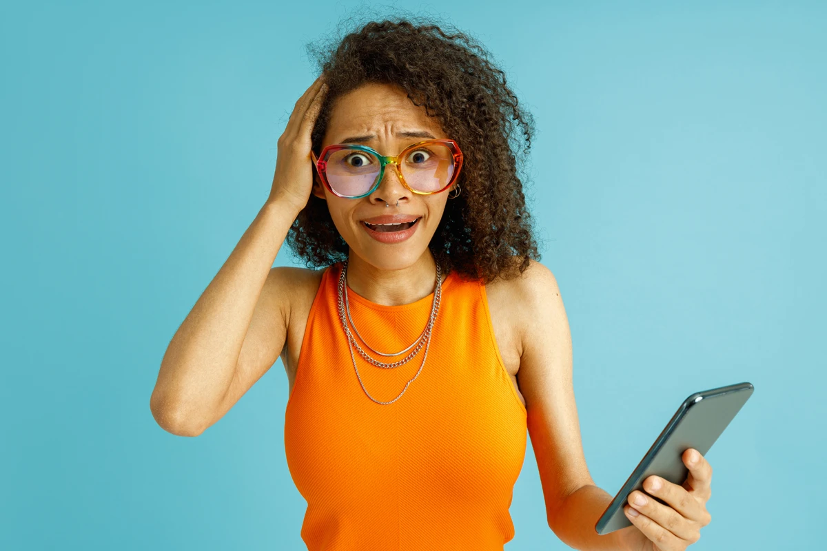 Shocked woman holding smartphone on blue background