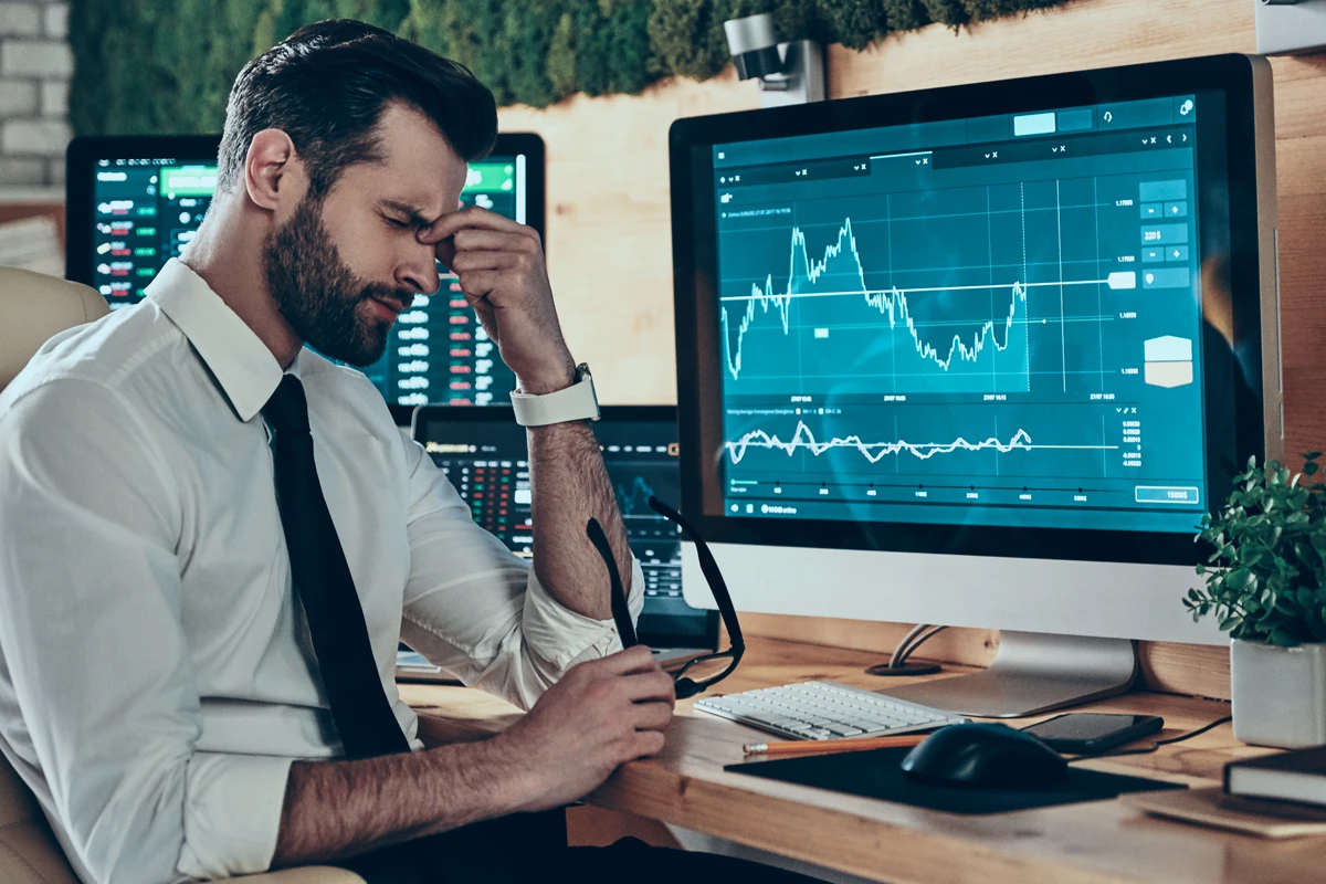 Stressed man analyzing financial charts on computer screens