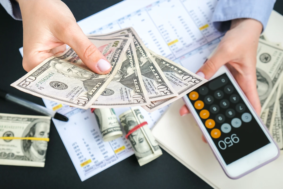 Person counting money with calculator on desk