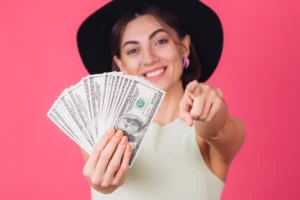 Woman in hat holding money and pointing at camera