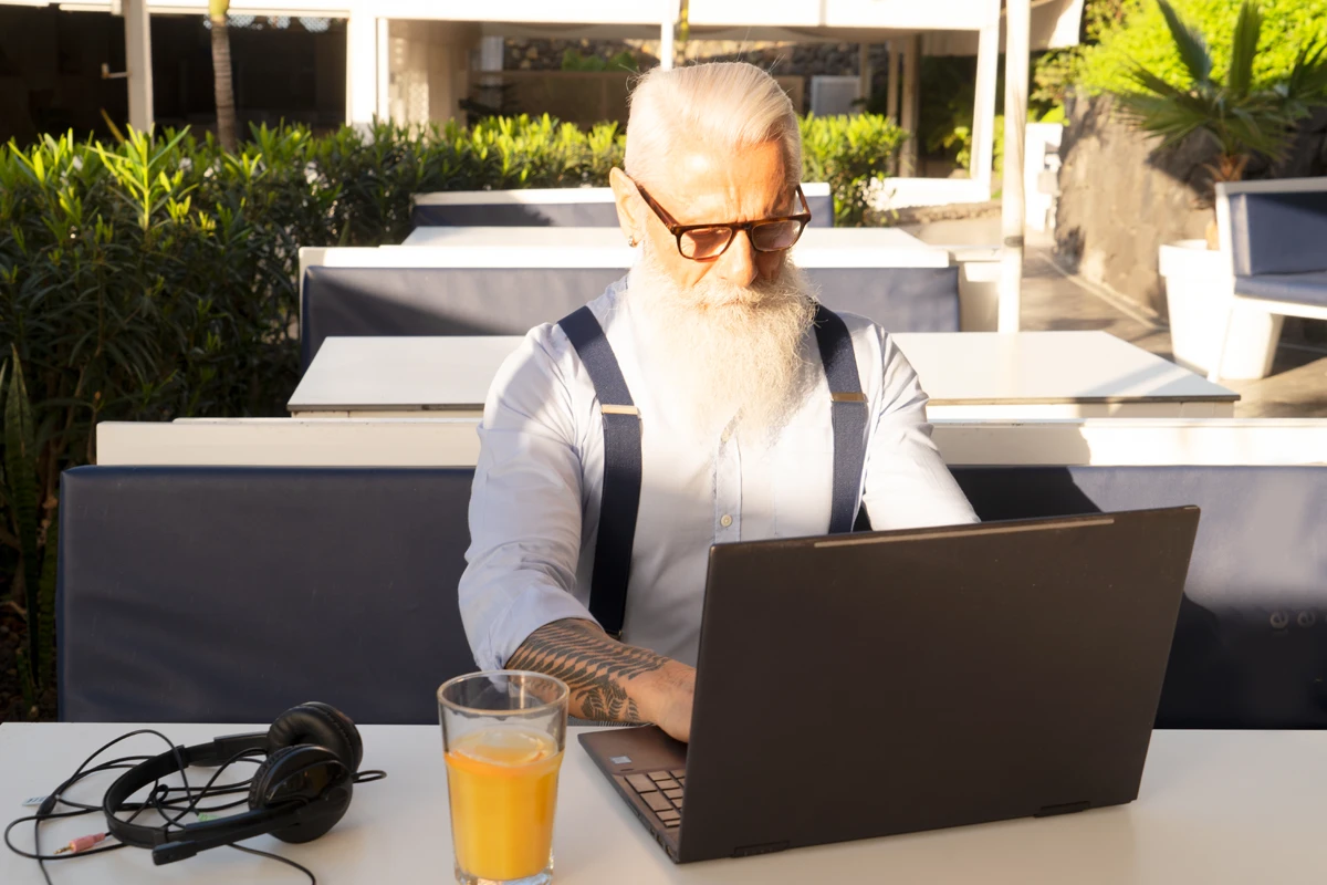 Elderly man with beard working on laptop outdoors