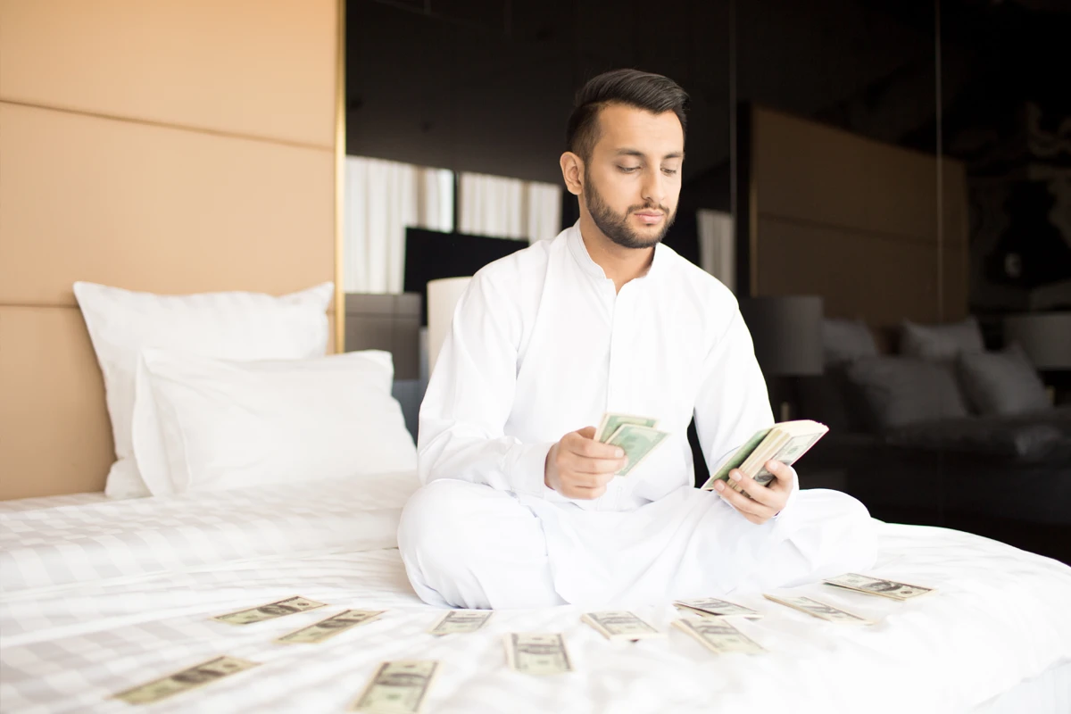 Man in white robe counting money on bed