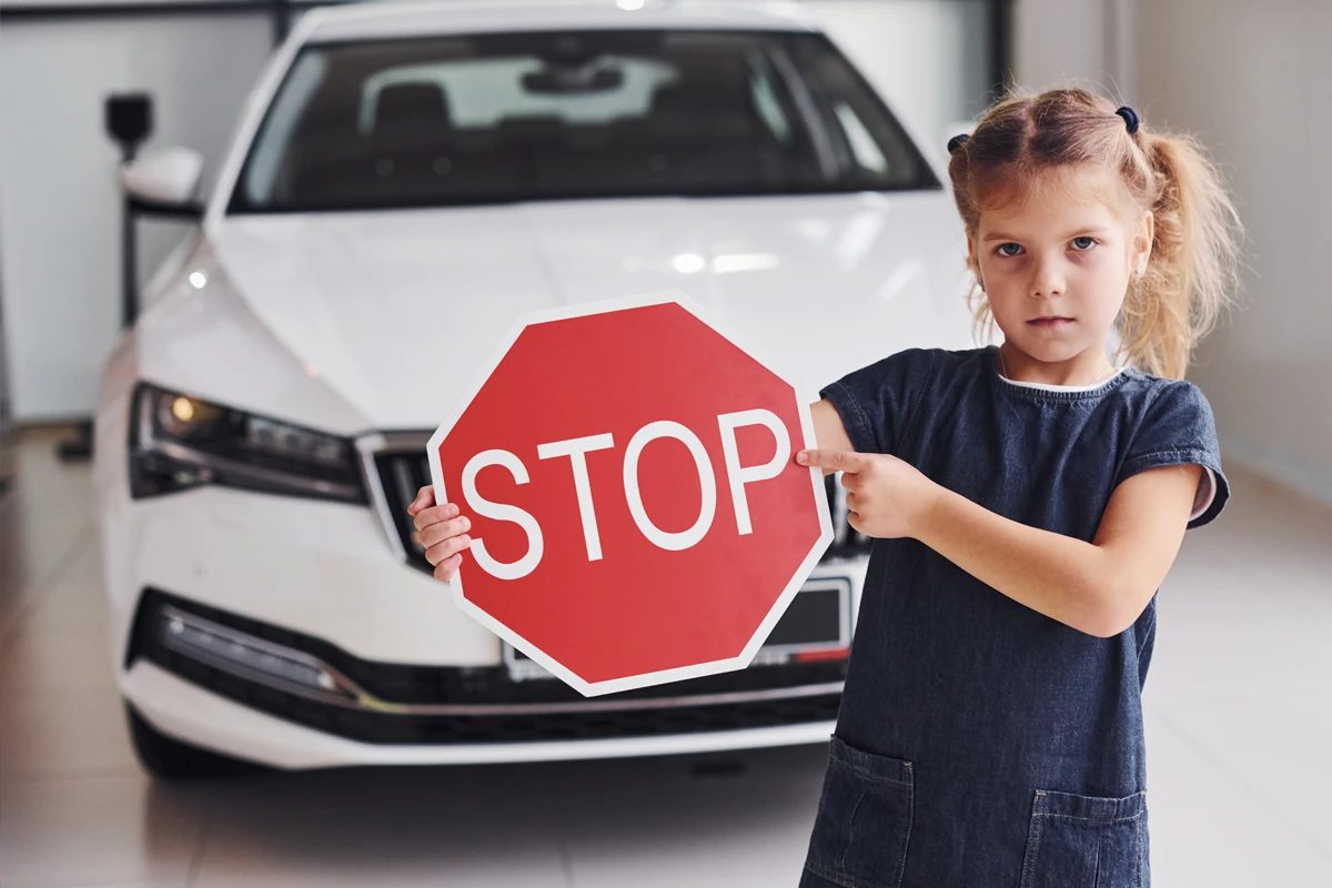 Young girl holding stop sign in front of car