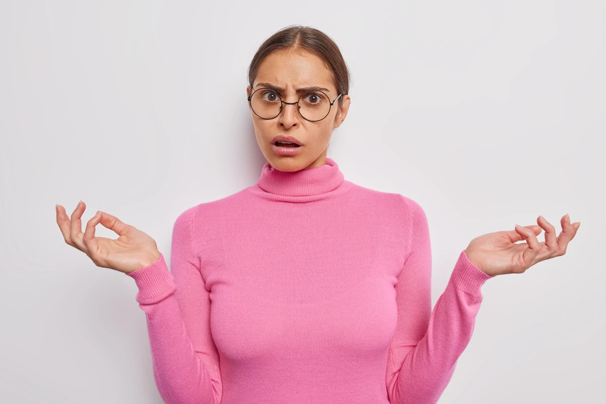 Confused woman in pink turtleneck gesturing with hands