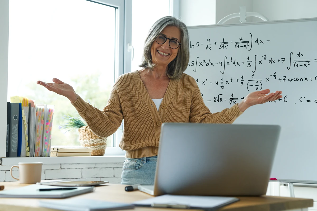 Smiling teacher explaining math at whiteboard in classroom