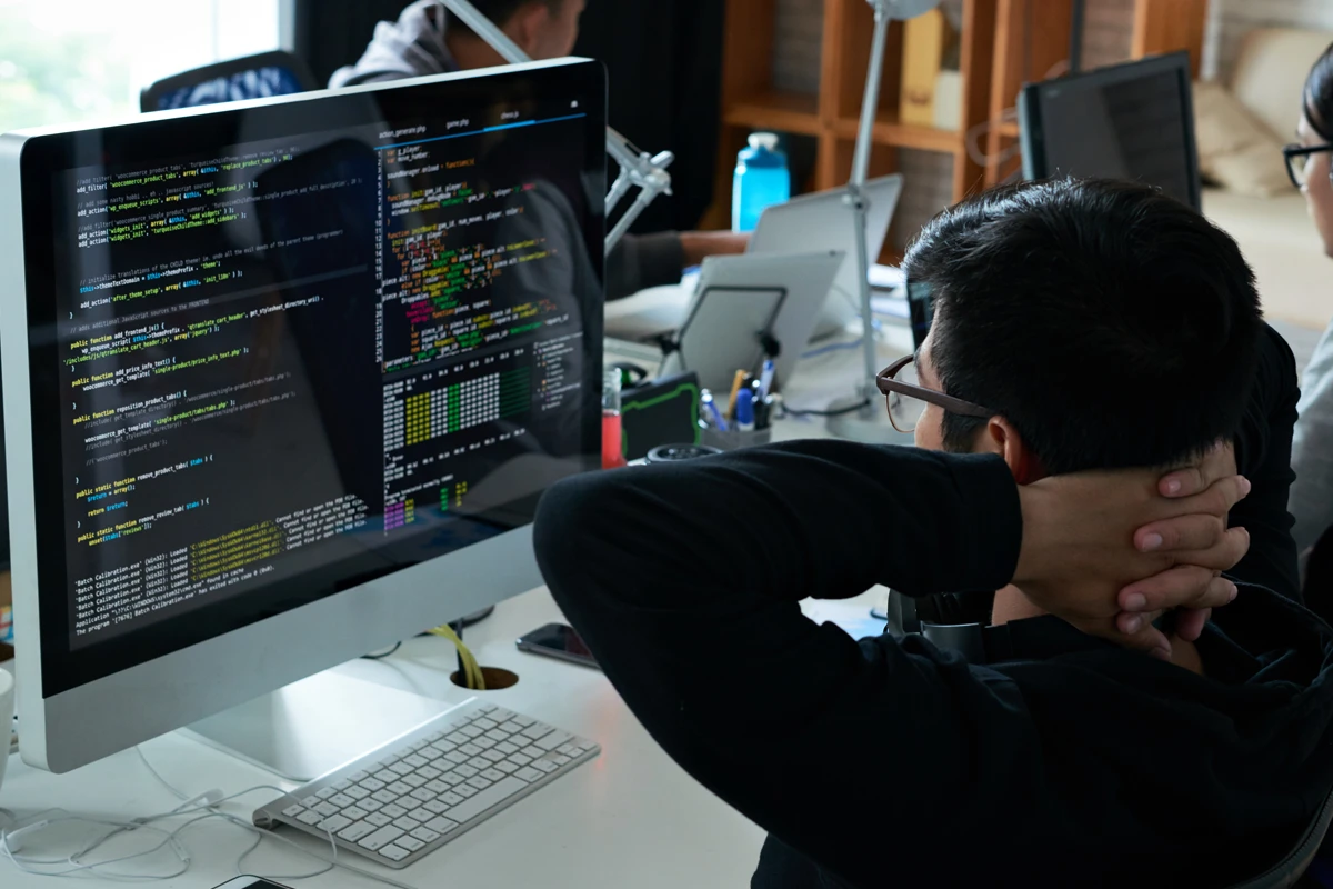 Programmer reviewing code on dual monitors in office