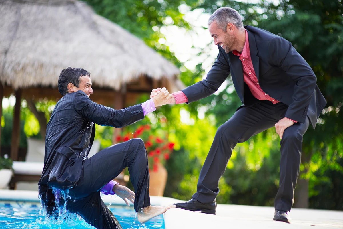 Men in suits playing by poolside, one falling in.