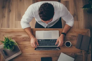 Man working on laptop at wooden desk, top view