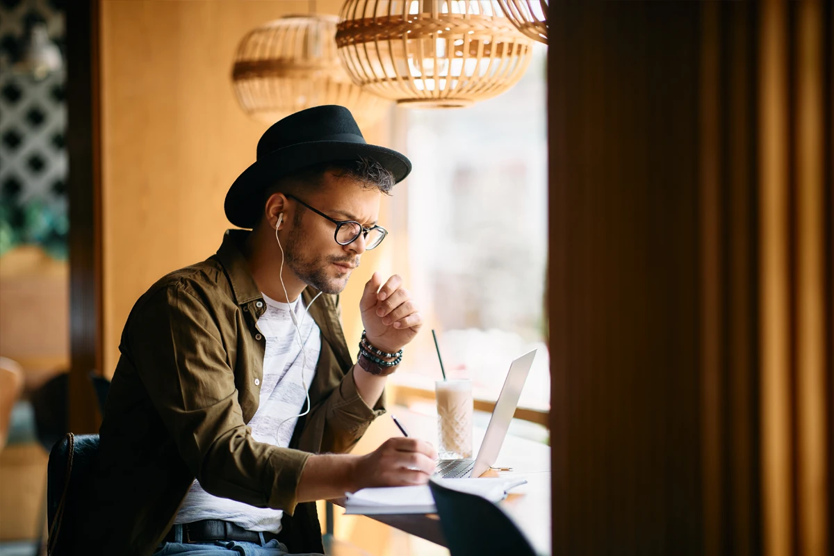 Man with hat writing in notebook at cafe