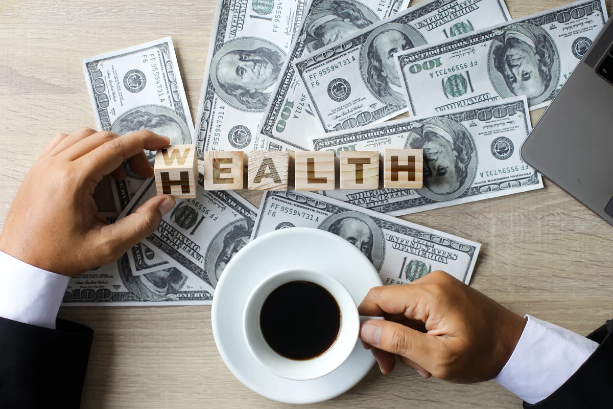 Person arranging 'WEALTH' blocks on money-strewn desk