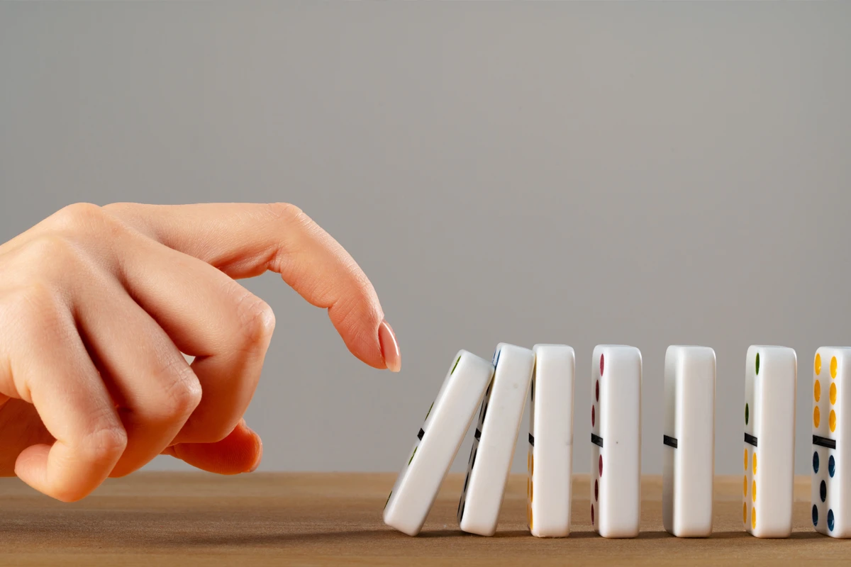 Hand tipping over a row of dominoes