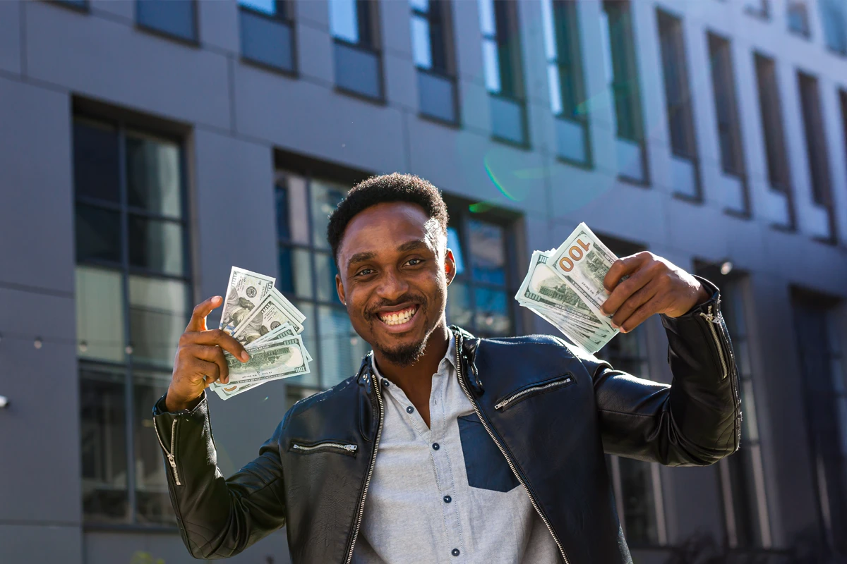 Smiling man holding money in front of modern building