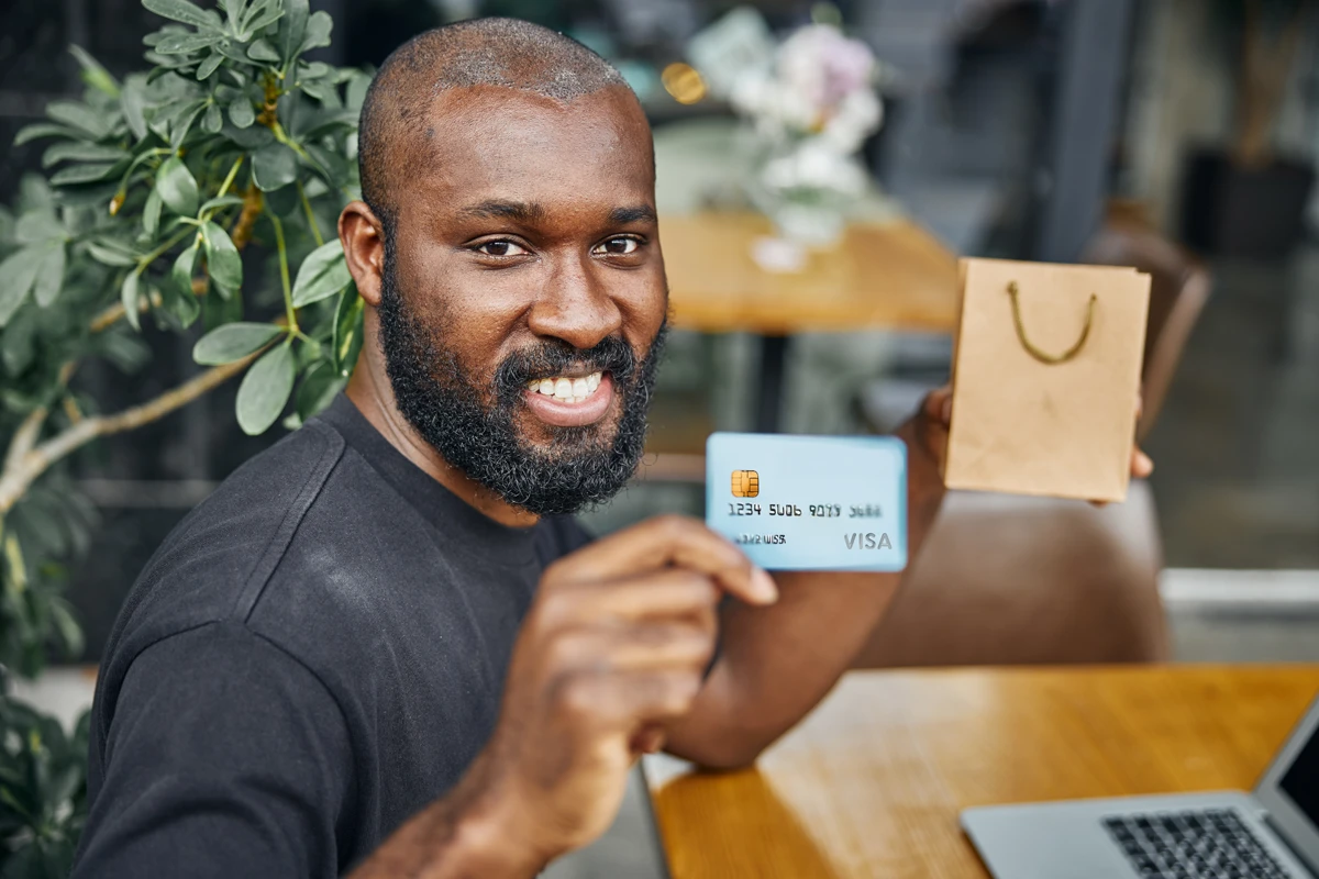 Man smiling, holding credit card and paper bag