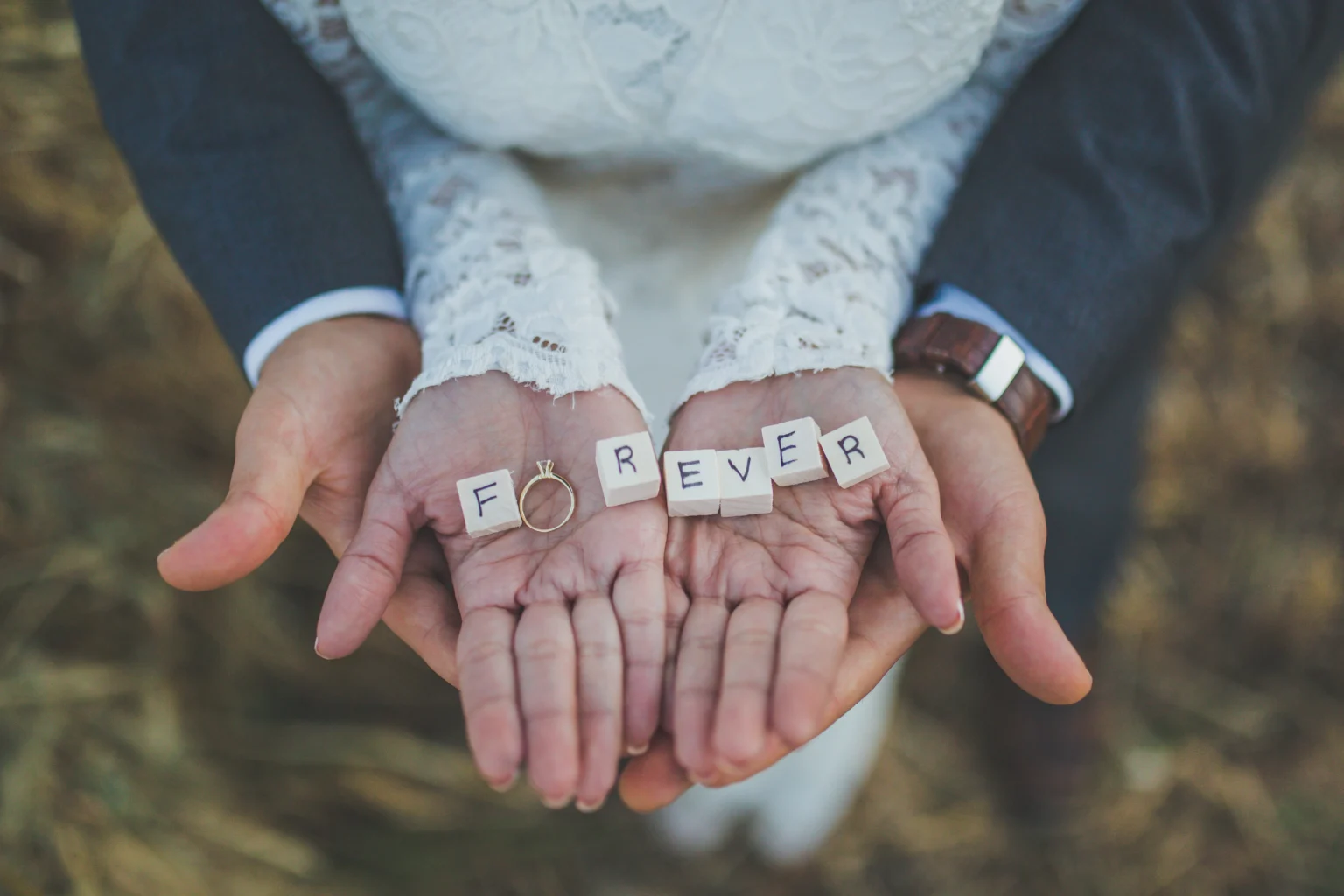 Couple holding hands with 'FOREVER' letter tiles and ring