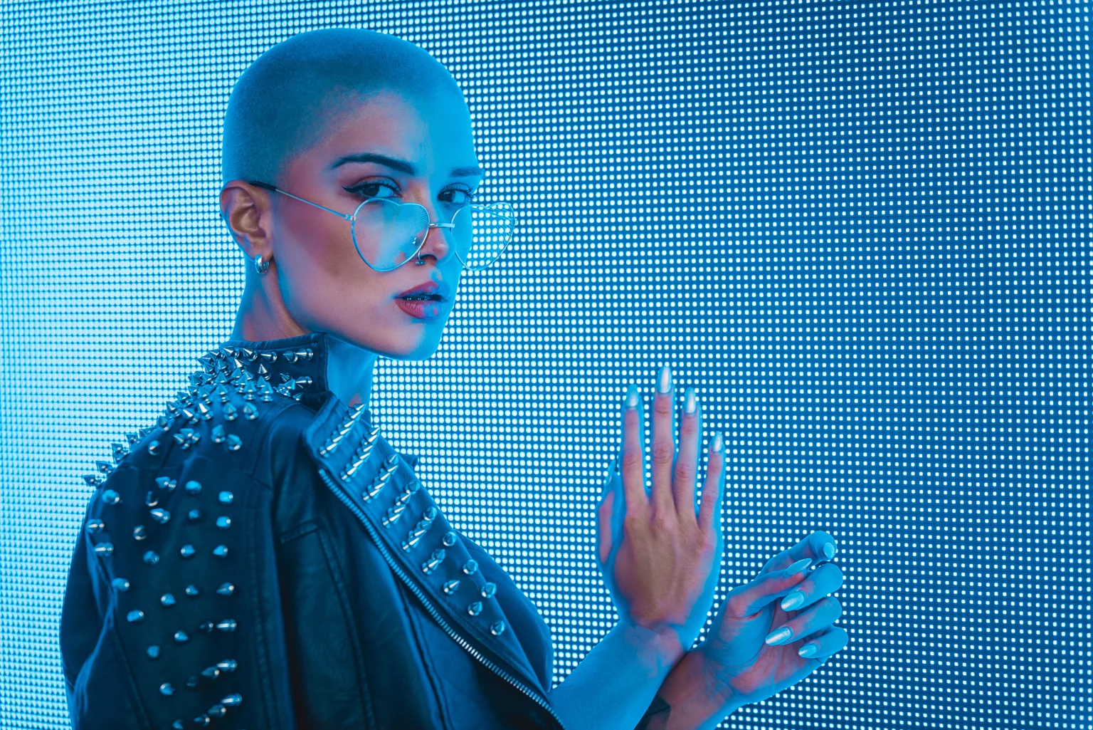 Woman with spiky jacket touching blue light wall
