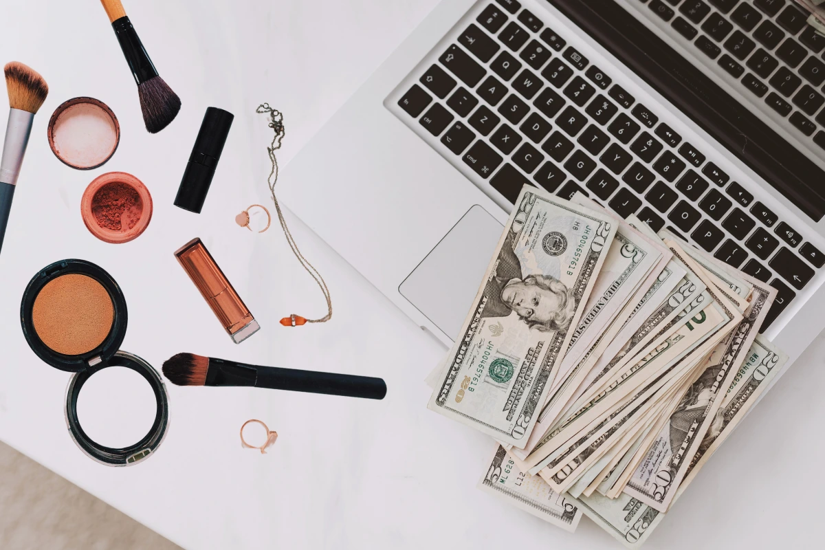 Cosmetics, jewelry, laptop, and cash on white desk