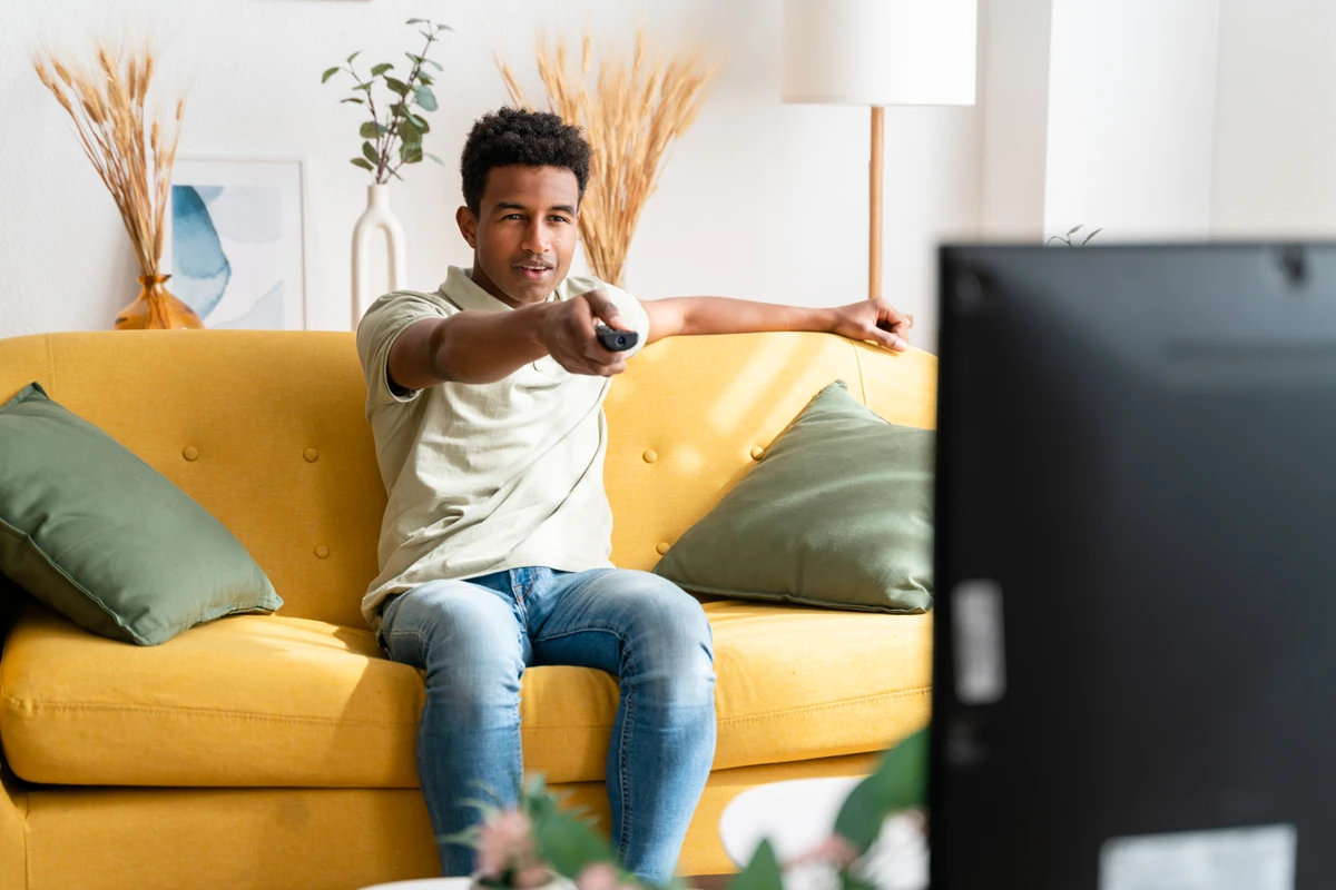 Man watching TV and using remote on yellow sofa
