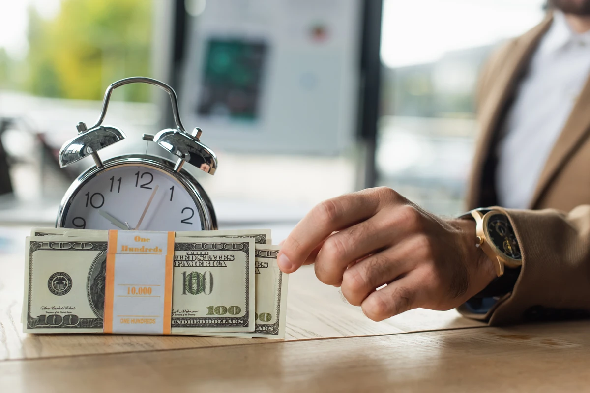 Man pushing cash towards alarm clock on table