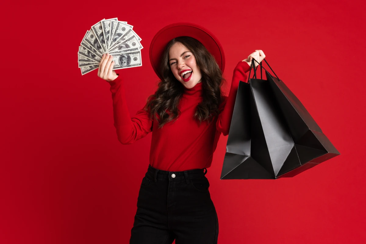 Joyful woman with money and shopping bags on red