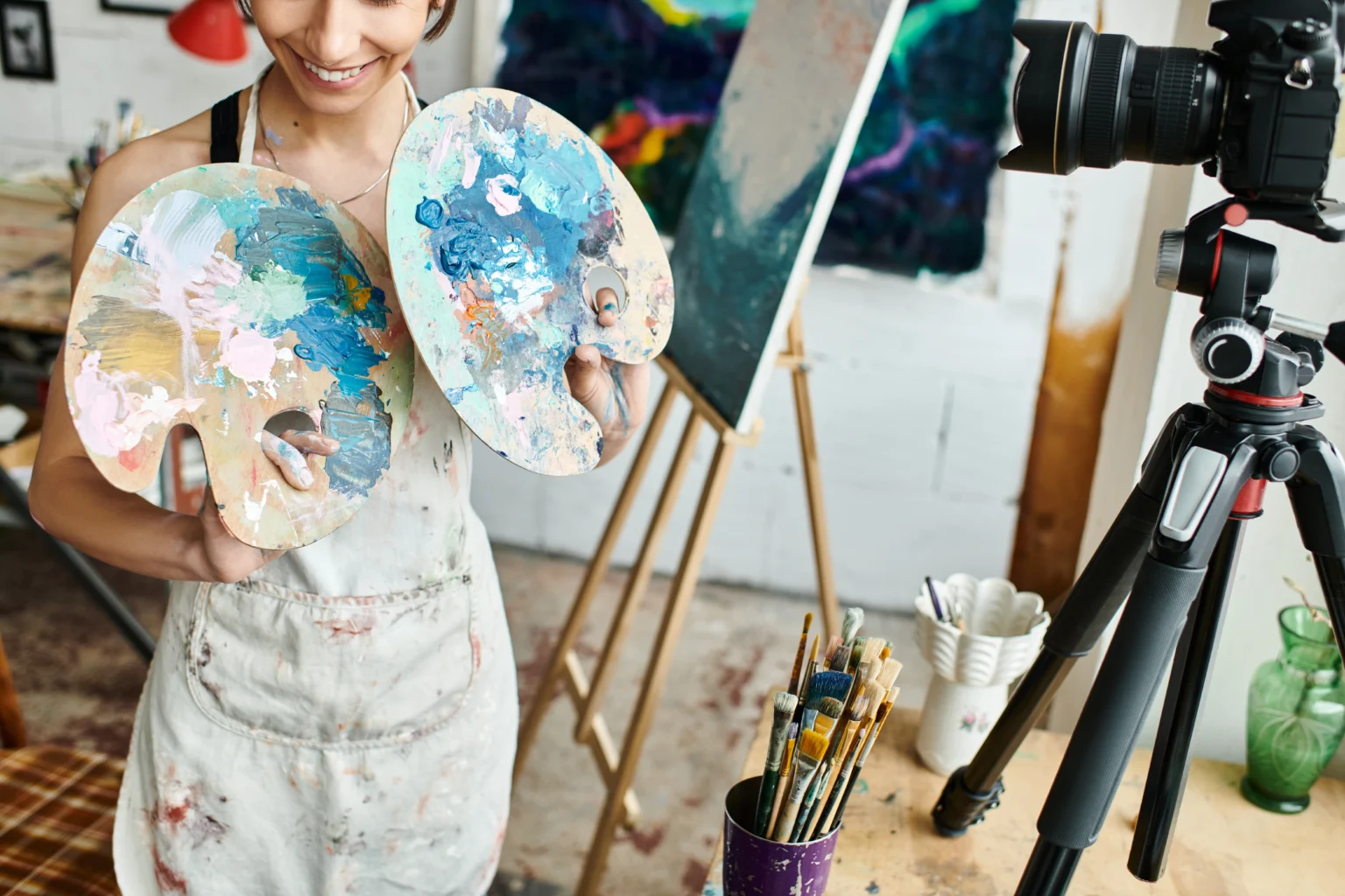 Artist holding colorful palettes in studio with camera
