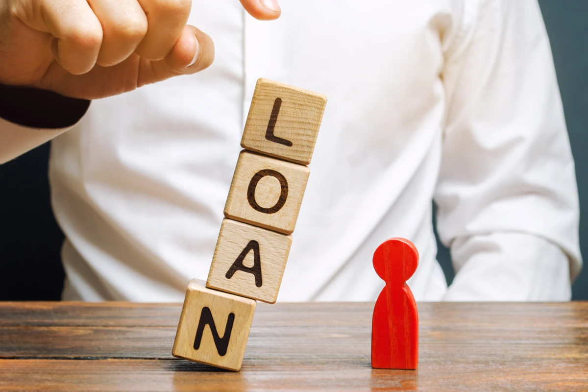 Person stacking 'LOAN' blocks beside red figure