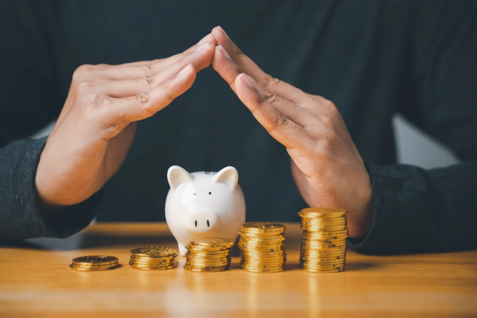 Person protecting piggy bank with coins