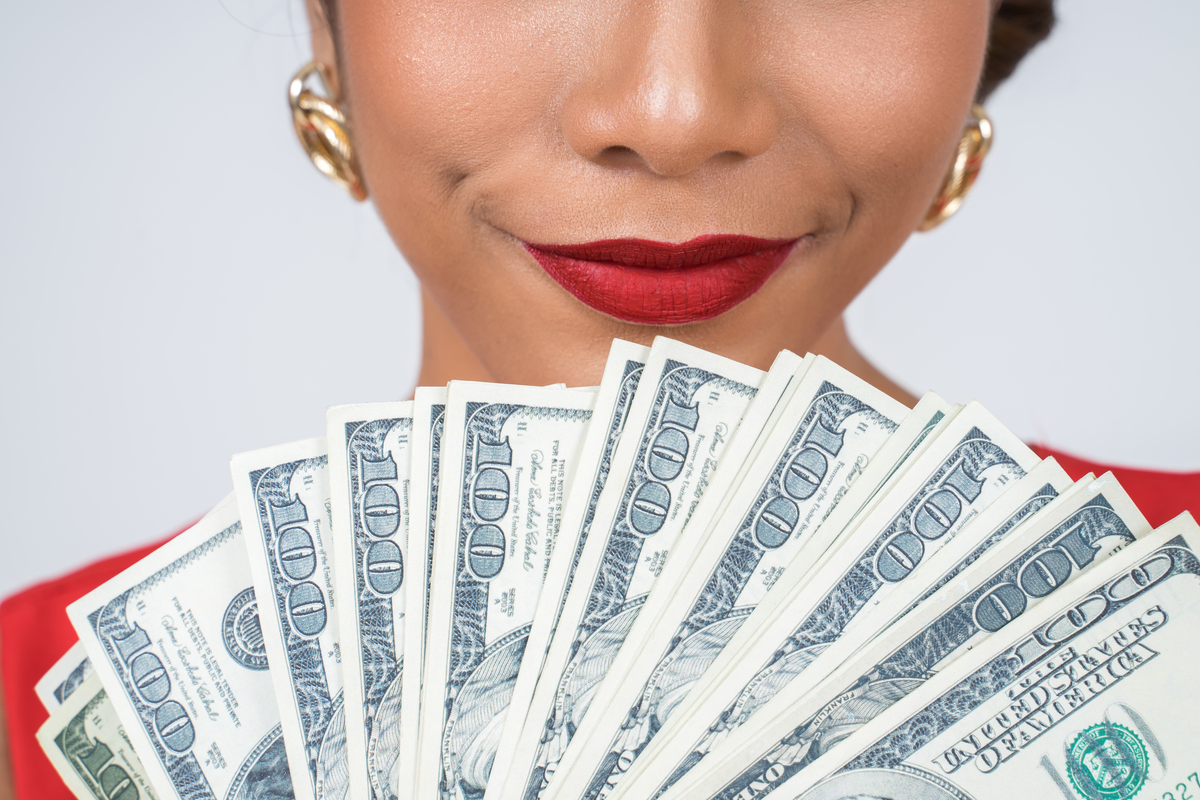Woman smiling holding a fan of hundred dollar bills