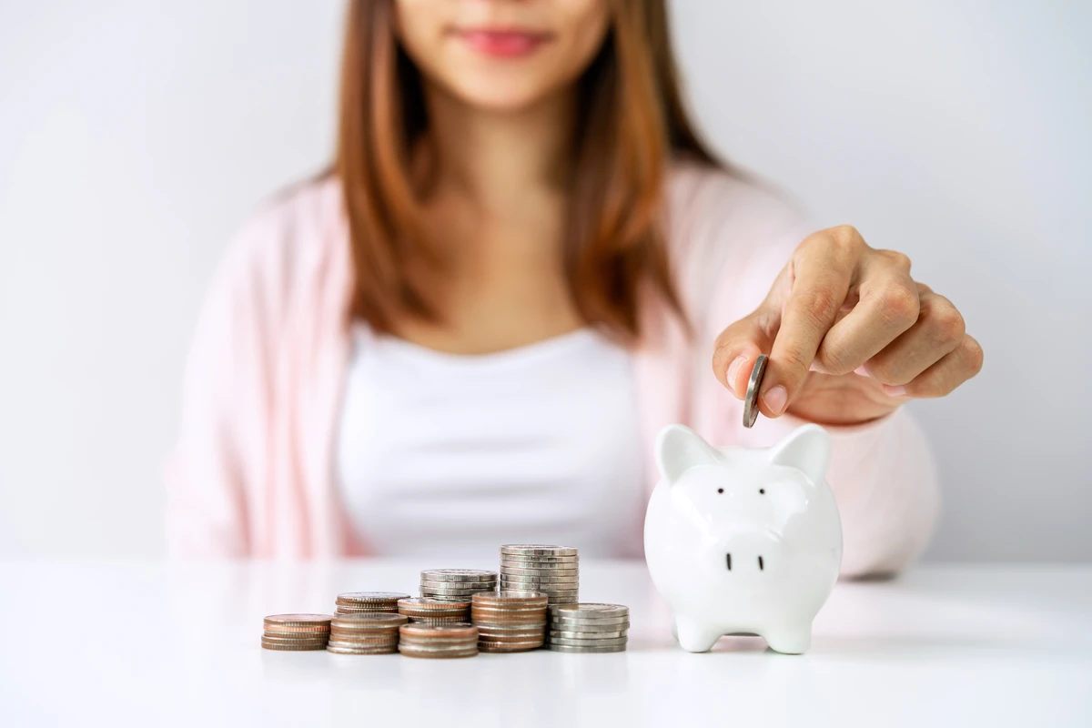 Woman depositing coin into piggy bank beside coin stacks