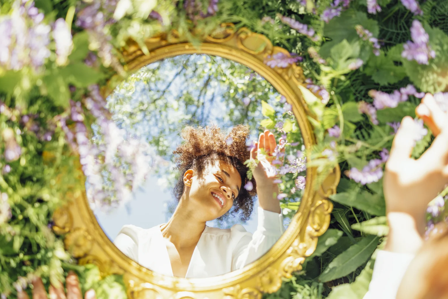 Woman admiring reflection in mirror surrounded by flowers.