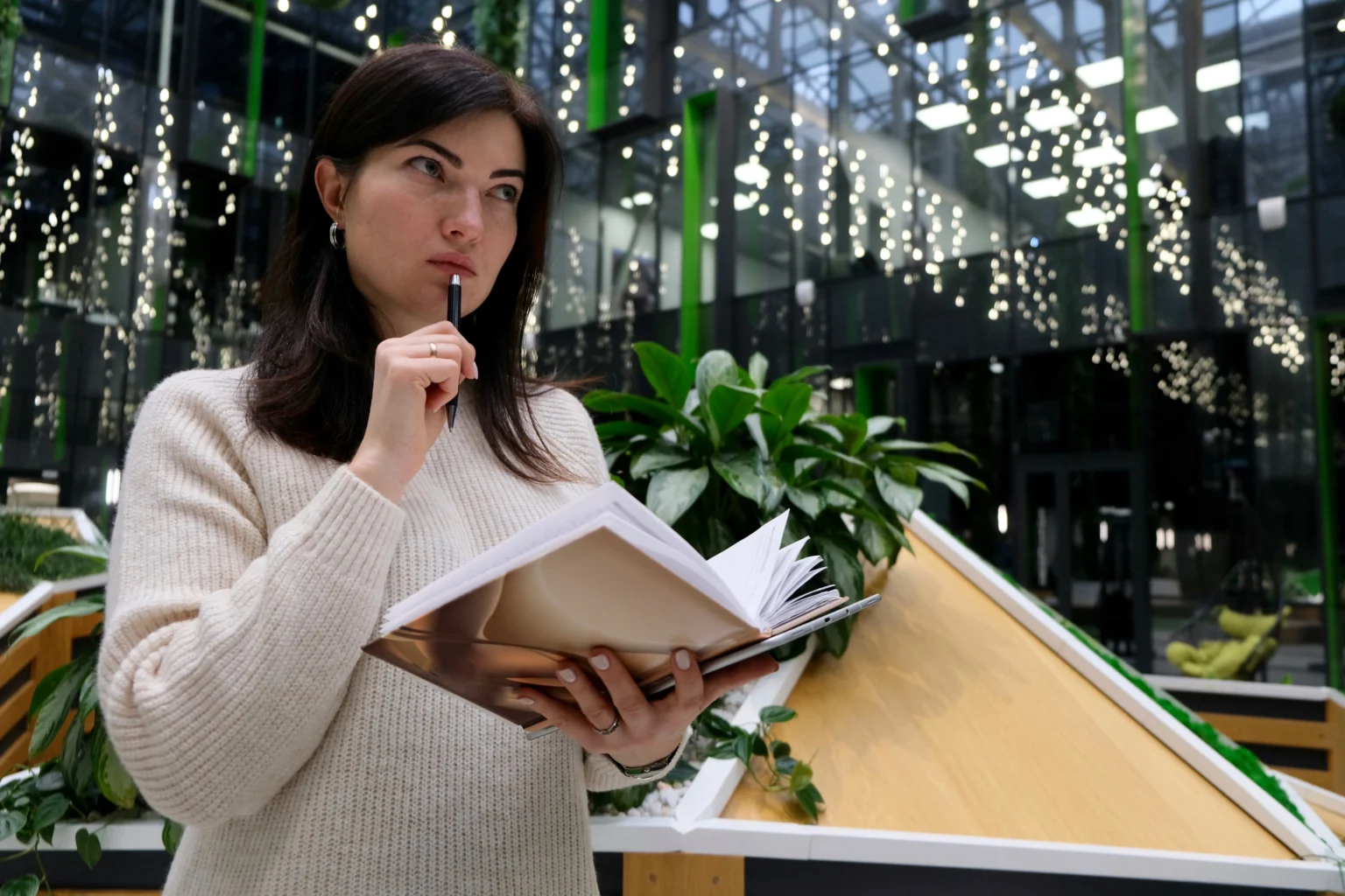 Woman pondering while holding notebook in modern atrium