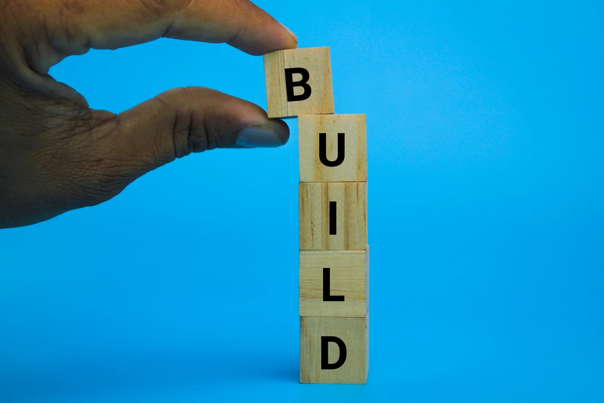 Hand stacking BUILD letters on wooden blocks against blue