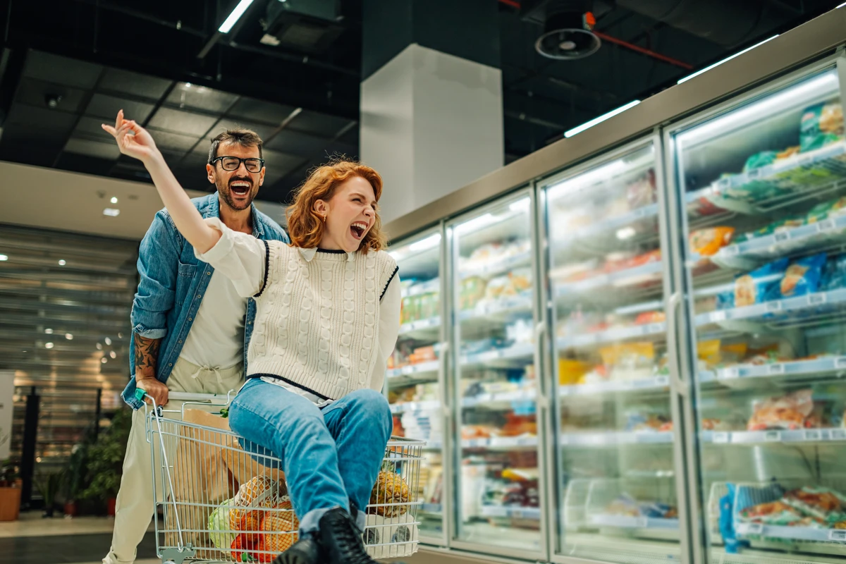 Joyful couple grocery shopping with woman in cart