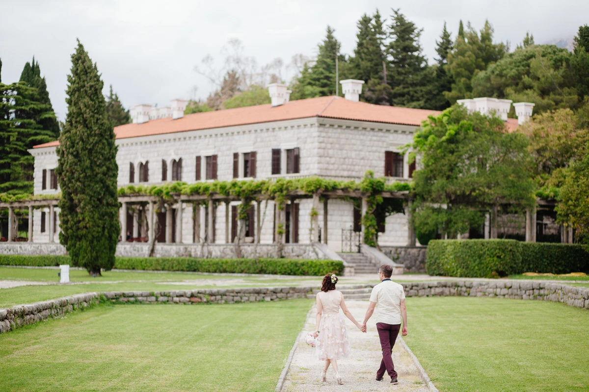 Couple walking towards stone mansion in lush garden