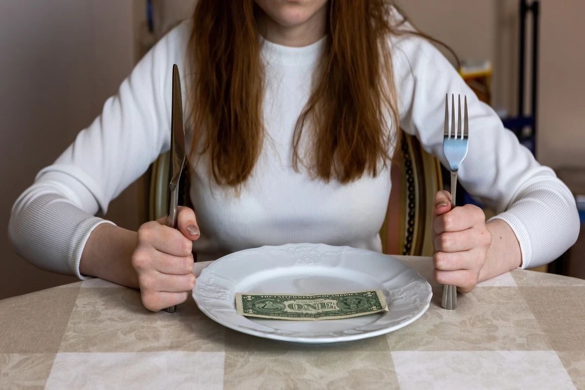 Woman holding utensils over plate with money