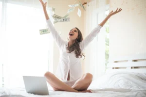 Woman celebrating with flying money sitting near laptop
