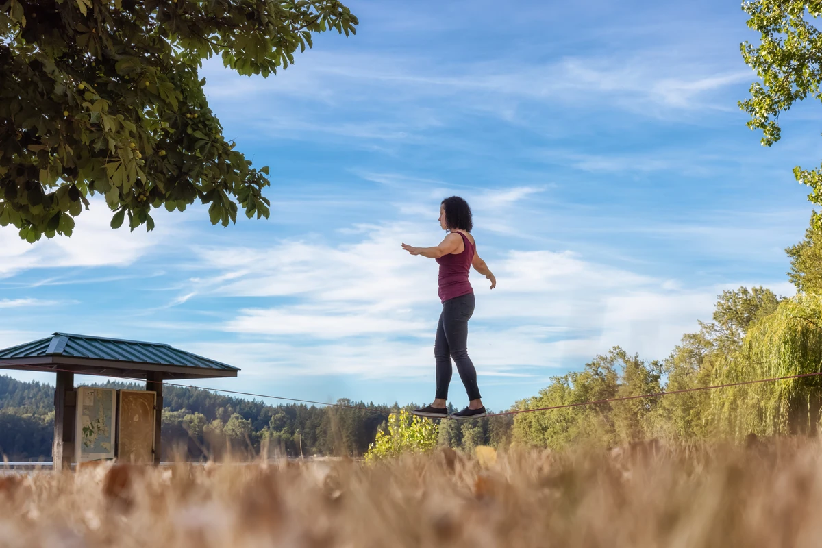 Woman slacklining outdoors near trees and a pavilion