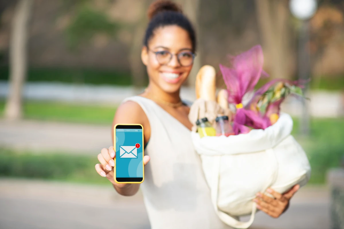 Woman showing phone app, holding grocery bag outdoors