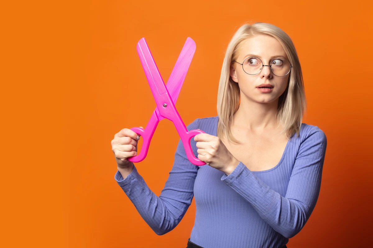 Woman holding large pink scissors, looking puzzled