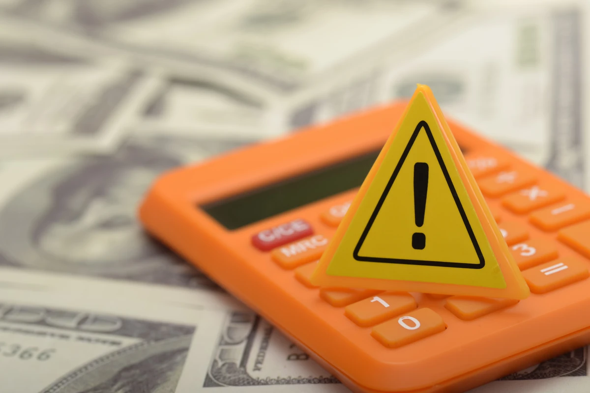 Yellow warning triangle on an orange calculator, placed on a background of dollar bills.