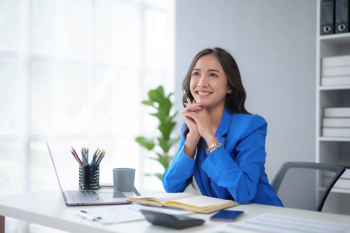 a woman sitting at a desk with a laptop and a pen